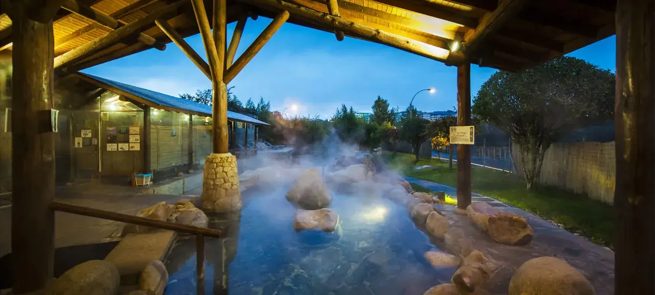 Dampfender Thermalpool unter einem Holzpavillon in Ourense, Spanien. Entspannung pur in der Abenddämmerung.