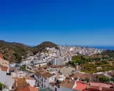Weiß getünchte Häuser schmiegen sich an einen Hügel in Frigiliana, Spanien. Der Blick reicht über die Dächer bis zum blauen Meer.