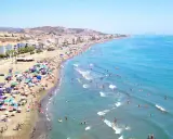 Ein belebter Strand in Rincón de la Victoria, mit vielen Sonnenschirmen, Menschen am Wasser und im Meer.