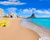 Sonne, Strand und Meer in Calpe, Spanien. Ein gelbes Wasserfahrrad wartet am Sandstrand, im Hintergrund die Stadt und der markante Felsen Peñón de Ifach. Ein echter Geheimtipp!
