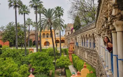 Frau blickt lächelnd aus einem Säulengang auf üppige Gärten mit Palmen. Ein versteckter Blick auf Sevilla, der Lust auf mehr macht. #sevilla #geheimtipps