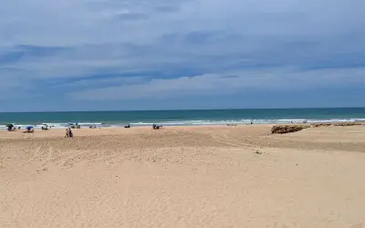 Weite Sandstrände und das Meer am Playa de Cortadura. Einige Menschen genießen den Tag unter Sonnenschirmen.