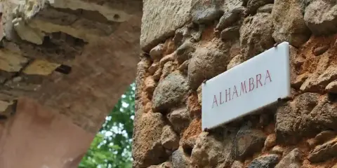 Schild "Alhambra" an einer alten Steinmauer, die zu einem Parkplatz führt.