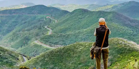 Mann mit Kamera genießt die Aussicht auf kurvige Straße in grünen Bergen. Perfektes Ziel für Wandern in Spanien.