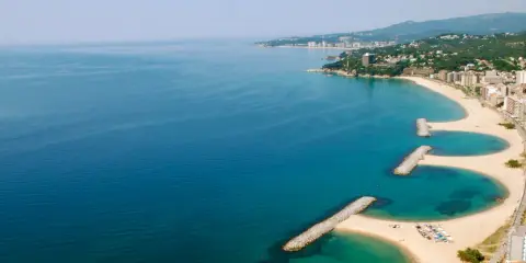 Bucht mit Wellenbrechern und Sandstränden in Calonge, Spanien. Die Küstenstadt erstreckt sich entlang des blauen Meeres.