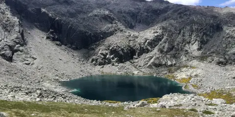 Ein tiefblauer Bergsee in der Sierra de Gredos, umgeben von felsigen Hängen und grünen Wiesen.