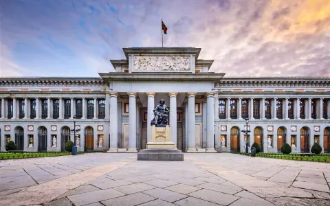 Das Prado Museum in Madrid, ein Meisterwerk der Architektur, mit einer Statue davor und einem dramatischen Himmel.