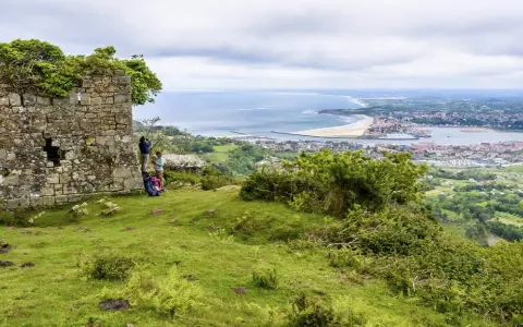 Zwei Wanderer genießen die Aussicht auf die Küstenstadt Irun, Spanien, von einer alten Ruine aus.