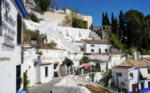Weiße Häuser und Terrassen im Sacromonte, Granada, mit Kopfsteinpflaster und blühenden Pflanzen.