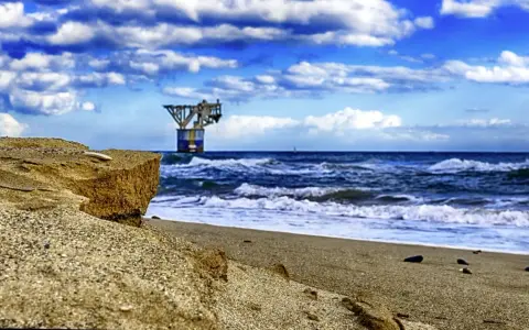 Sandige Klippen am playa del cable, mit einer Plattform im Meer unter dramatischem Himmel.