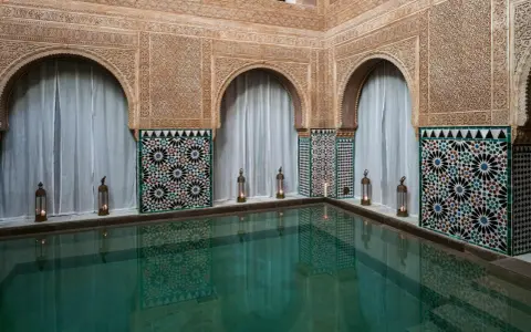Ein ruhiger Pool im Hammam Al Andalus, umgeben von kunstvollen Fliesen und Schnitzereien, mit Kerzenlicht.