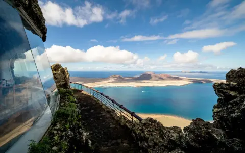 Blick vom Mirador del Río auf das Tal der tausend Palmen Lanzarote. Blaue See, Inseln und eine Hütte mit Glasfront.