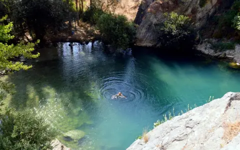 Ein Mann schwimmt im türkisfarbenen Wasser der Cueva del Gato, umgeben von Felsen und üppiger Vegetation.