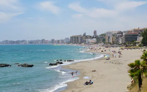 Sonniger Benalmadena Strand mit vielen Menschen, bunten Sonnenschirmen und dem türkisfarbenen Meer.