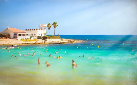 Sonnige Küste in Costa Calida, Spanien, mit vielen Menschen, die im türkisfarbenen Meer schwimmen.
