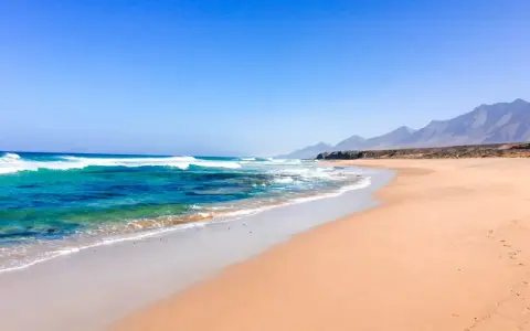 Weite Sandstrände und türkisfarbenes Meer, die an die Meerenge von Gibraltar erinnern. Berge im Hintergrund.
