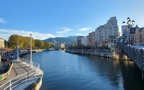 Blick auf den Bilbao Fluss mit Gebäuden und einer Brücke im Hintergrund.