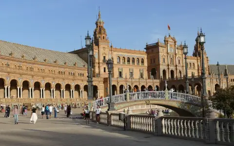 Familien genießen einen sonnigen Tag auf der Plaza de España in Sevilla. Kinder lachen, während sie über die Brücke spazieren, die über einen Kanal führt.