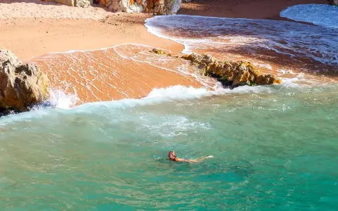 Eine Frau schwimmt im türkisfarbenen Meer vor einer sandigen Bucht in Palamós, Spanien.