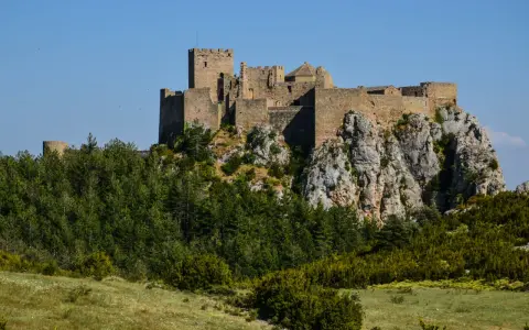 Das Castillo de Loarre thront majestätisch auf einem Felsen, umgeben von grünen Wäldern und unter blauem Himmel.