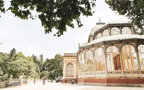 Ein sonniger Tag im Retiro Park. Menschen spazieren vor dem Palacio de Cristal, einem beeindruckenden Glaspalast.