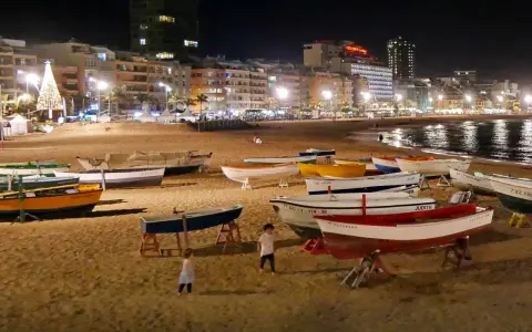 Boote am Strand bei Nacht, beleuchtete Stadt und Weihnachtsbaum. Selbst im Spanien Winter ist die Temperatur angenehm für einen Spaziergang.