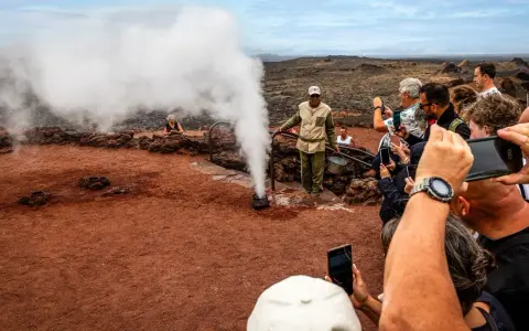 Touristen bestaunen im Nationalpark Timanfaya eine Dampf-Demonstration. Ein Führer gießt Wasser in ein Loch, das sofort zu Dampf wird.