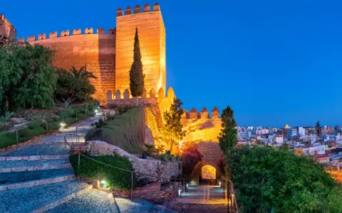 Die Alcazaba von Almería erstrahlt im Abendlicht. Beleuchtete Wege führen durch Gärten zur imposanten Festung.