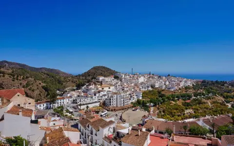 Weiß getünchte Häuser schmiegen sich an einen Hügel in Frigiliana, Spanien. Der Blick reicht über die Dächer bis zum blauen Meer.