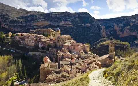 Malerisches Dorf Albarracín, Spanien, schmiegt sich an steile Felsen. Ein Weg führt durch grüne Hügel zum historischen Ortskern.