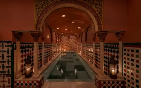Ein prachtvoller Hammam in Granada mit einem langen Pool, umgeben von kunstvollen Kacheln und Säulen, beleuchtet von Kerzen.