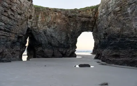 Felsbögen am Praia das Catedrais, die wie Kathedralen wirken, mit Sand und Meer im Hintergrund.