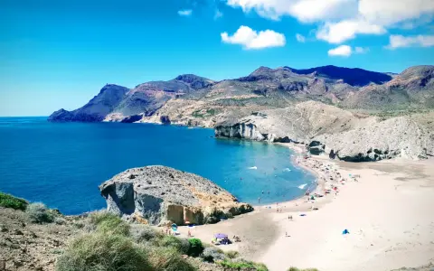 Sonnige playa de mónsul mit türkisfarbenem Wasser, Bergen und vielen Badegästen.