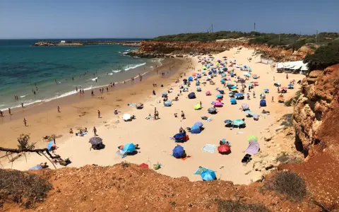 Sonniger Tag am playa fuente del gallo mit vielen bunten Sonnenschirmen und Badegästen im türkisfarbenen Meer.