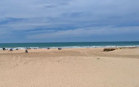Weite Sandstrände und das Meer am Playa de Cortadura. Einige Menschen genießen den Tag unter Sonnenschirmen.