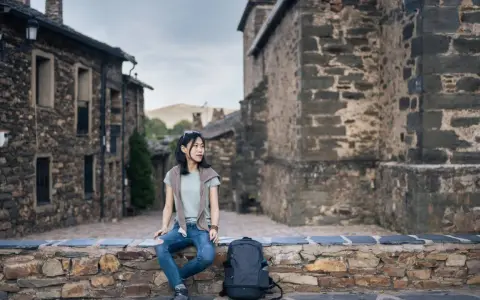 Junge Frau sitzt auf Steinmauer in historischem Dorf in Guadalajara, Spanien.