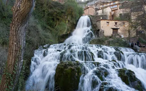 Tosender Wasserfall stürzt über Felsen, Häuser von Orbaneja del Castillo schmiegen sich an den Hang.