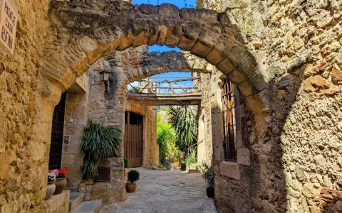 Antiker Durchgang in Pals, Spanien, mit steinernen Bögen und mediterraner Vegetation.