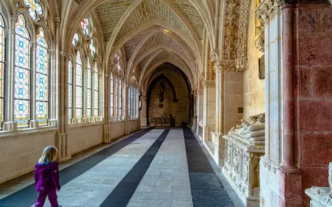 Ein Kind erkundet die gotischen Gänge der Burgos Kathedrale, vorbei an bunten Glasfenstern und kunstvollen Sarkophagen.
