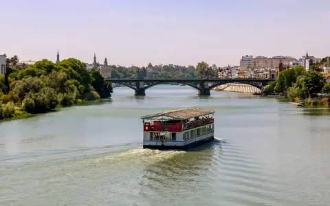 Ein Ausflugsboot fährt auf dem Guadalquivir, dem sevilla fluss, unter einer Brücke hindurch.