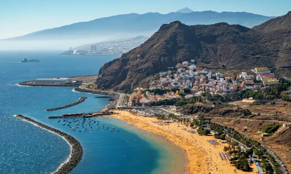Bunte Häuser schmiegen sich an steile Hänge, während ein goldener Strand und das blaue Meer die Küste von Spanien zieren. Im Hintergrund erheben sich majestätische Berge.