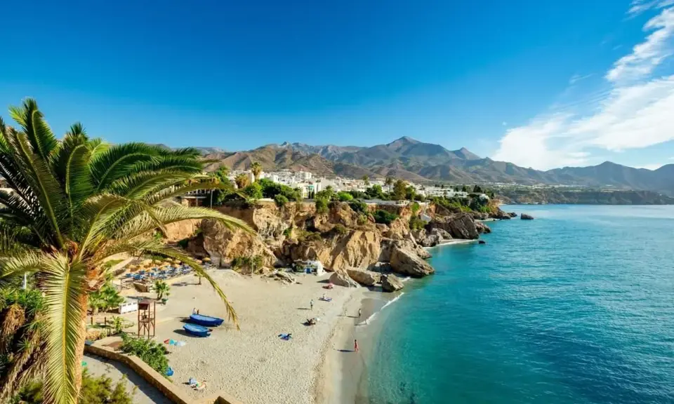 Sonnige playa de calahonda mit Palmen, weißem Sand, türkisfarbenem Meer und Bergen im Hintergrund.