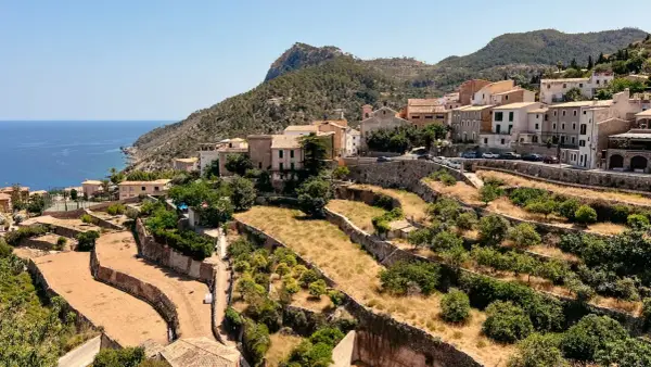 Terrassierte Felder und Häuser schmiegen sich an die Hänge des Tramuntana Gebirges, mit dem blauen Meer im Hintergrund.