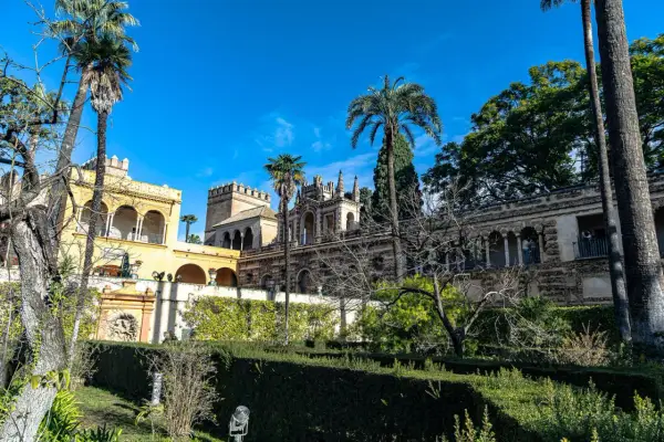 Sonniger Tag im Alcázar von Sevilla. Palmen ragen über kunstvoll verzierte Gebäude und gepflegte Gärten.