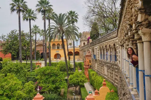 Frau blickt lächelnd aus einem Säulengang auf üppige Gärten mit Palmen. Ein versteckter Blick auf Sevilla, der Lust auf mehr macht. #sevilla #geheimtipps