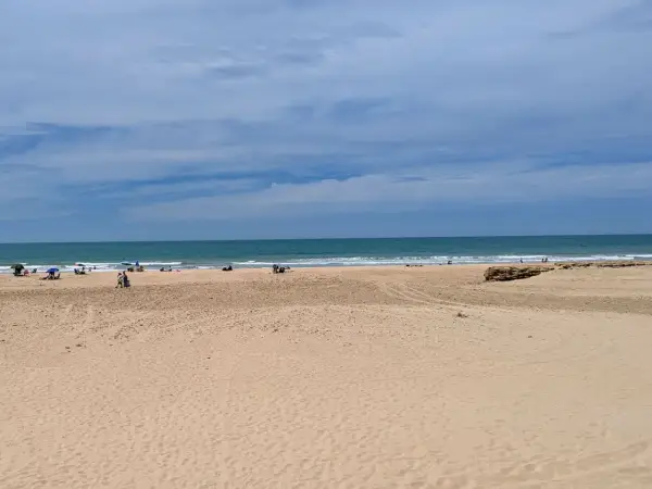 Weite Sandstrände und das Meer am Playa de Cortadura. Einige Menschen genießen den Tag unter Sonnenschirmen.