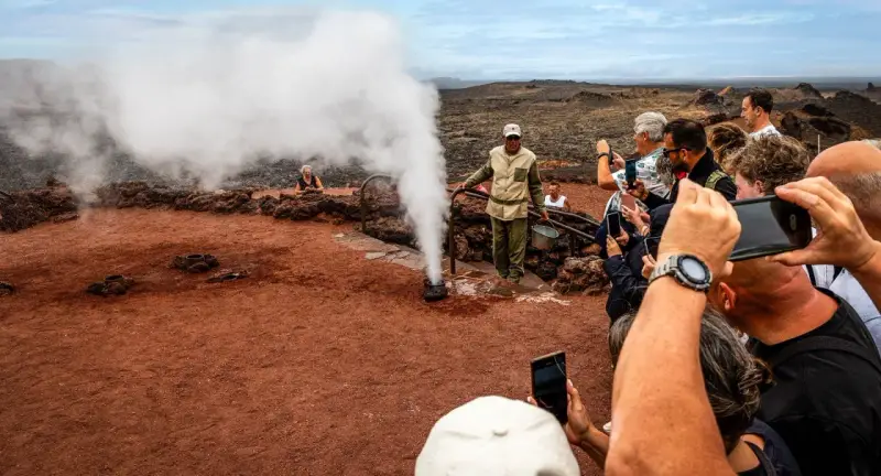 Touristen bestaunen im Nationalpark Timanfaya eine Dampf-Demonstration. Ein Führer gießt Wasser in ein Loch, das sofort zu Dampf wird.